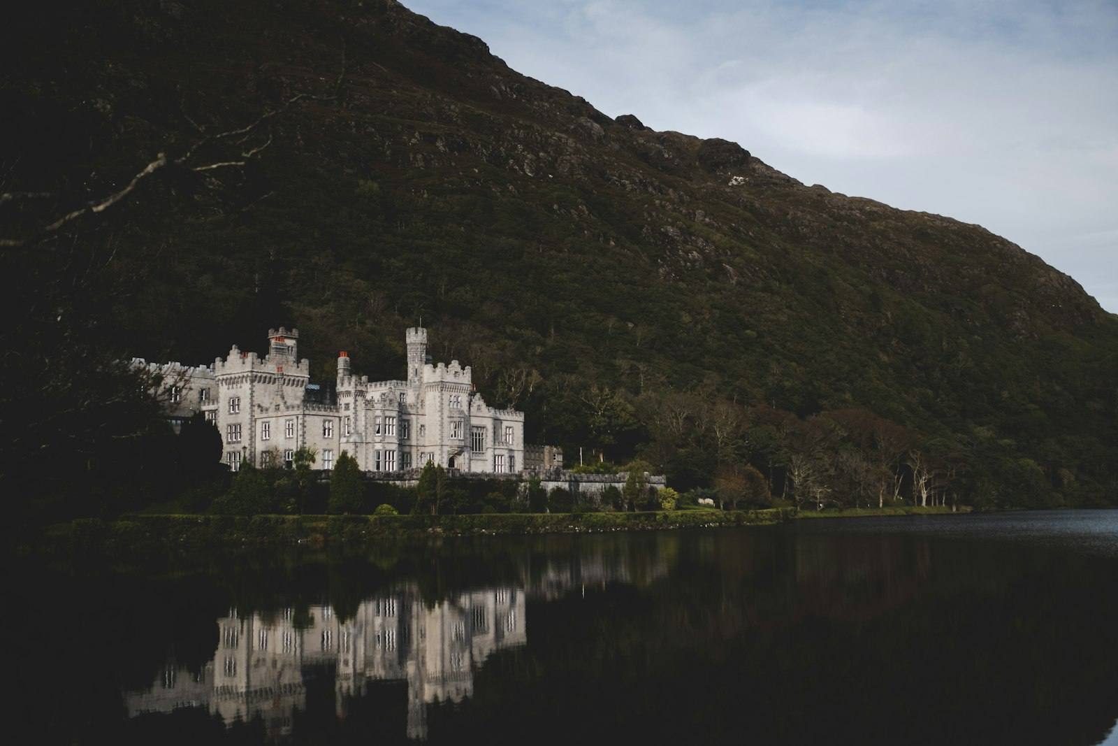 Kylemore Abbey reflected in the still lough under a dark mountainside, Conamara
